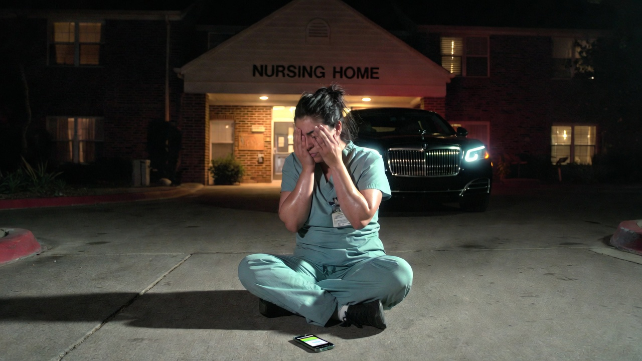 CNA sitting on the ground outside a nursing home at night, face in hands, crying — earns $33,280 a year